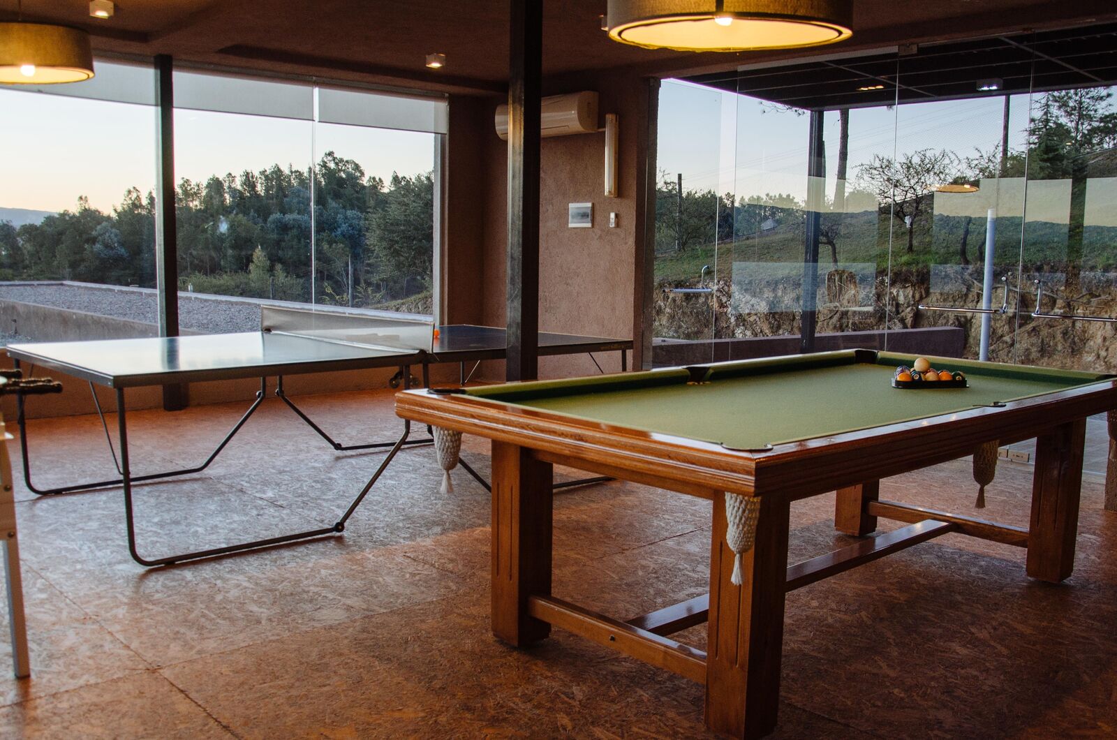 Mesa de sinuca e mesa de pingue-pongue na sala de jogos, com janelas para o parque
